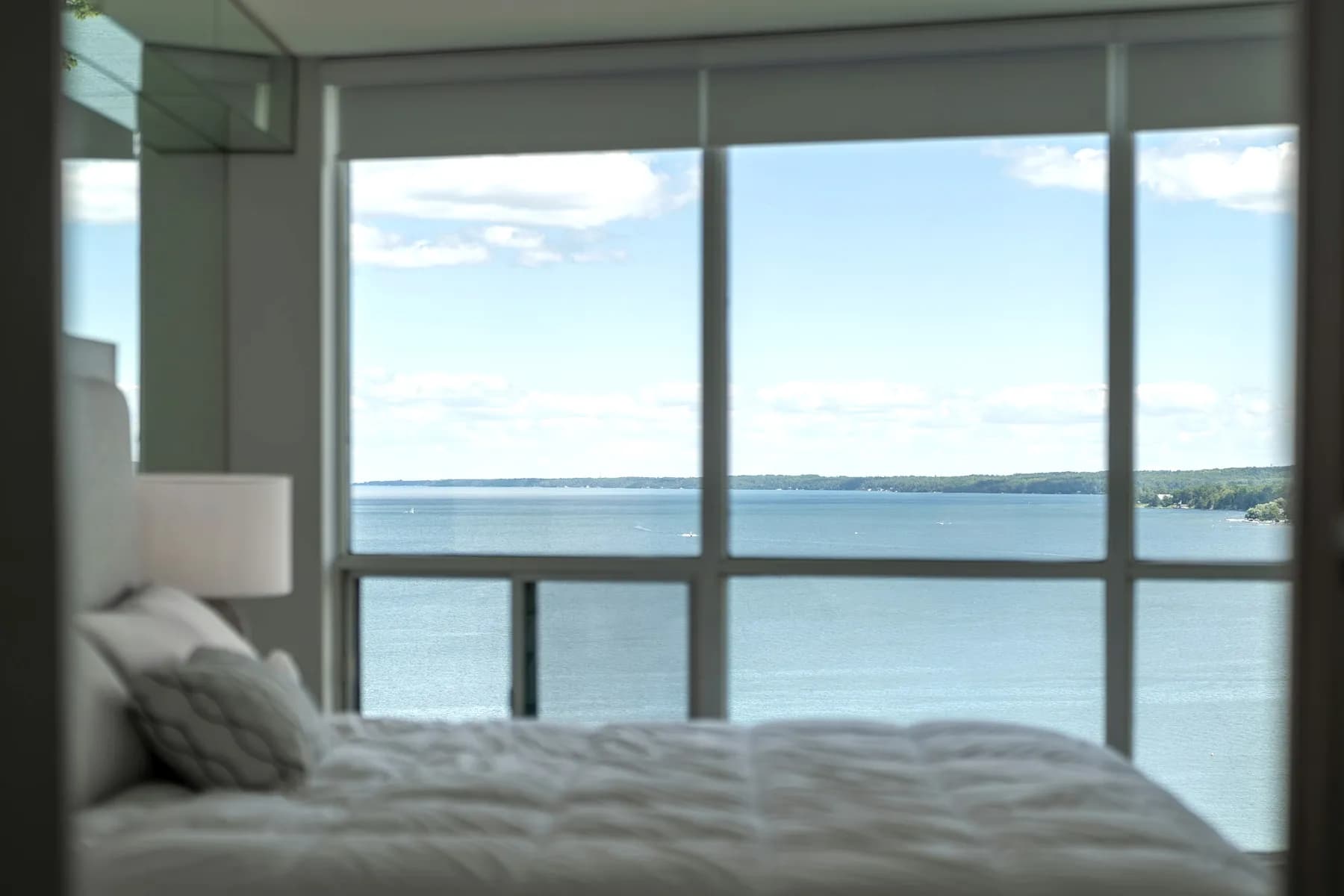 Chambre épurée aux tons clairs, avec une grande baie vitrée ouverte sur l'eau.